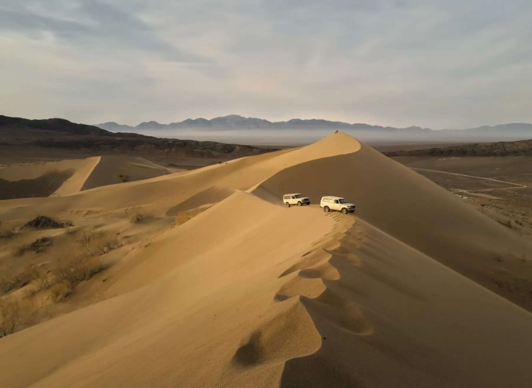 Two jeeps crossing the Altyn-Emel dunes at sunrise