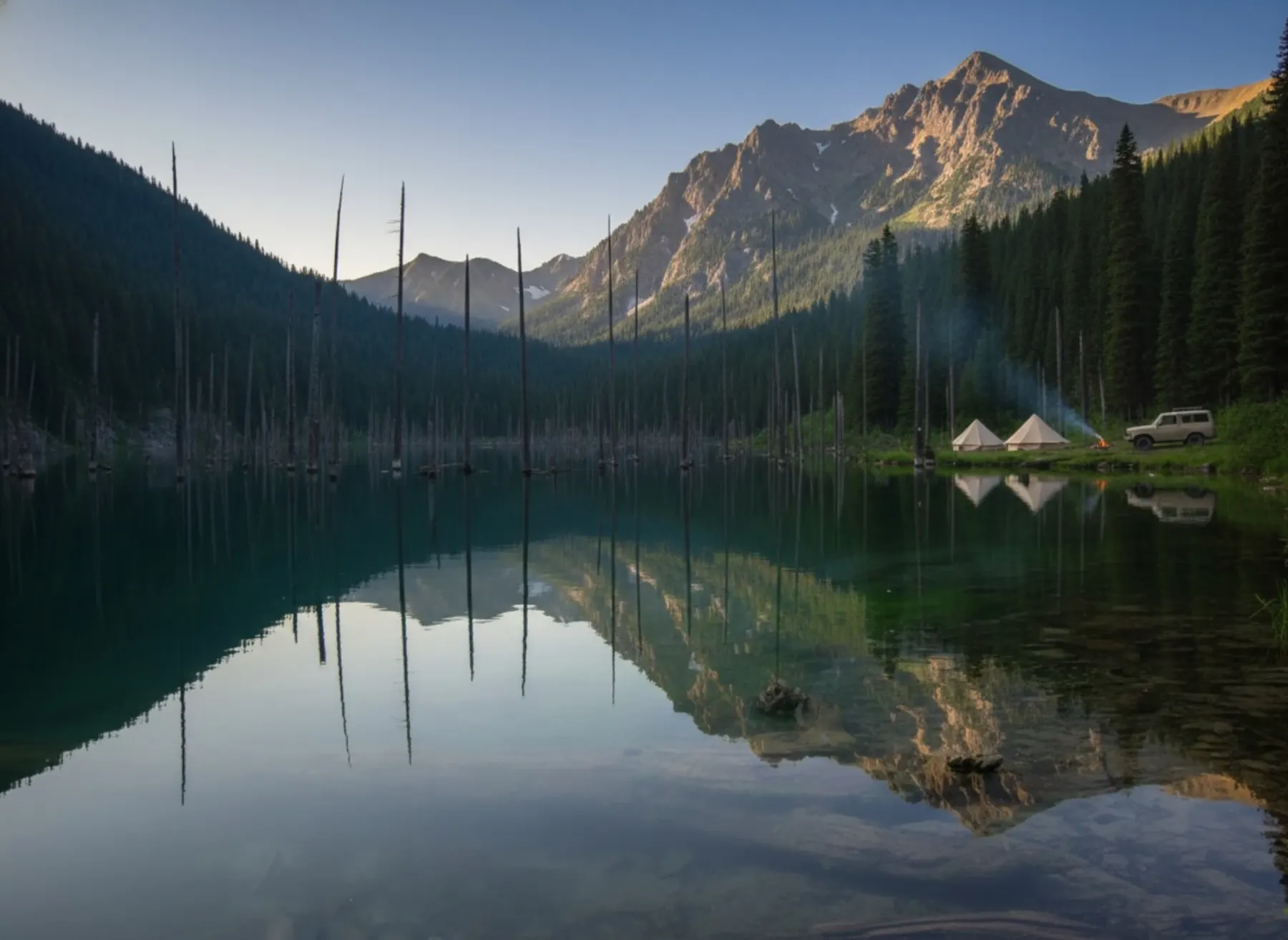 Canvas camp beside an alpine lake under snow-capped peaks